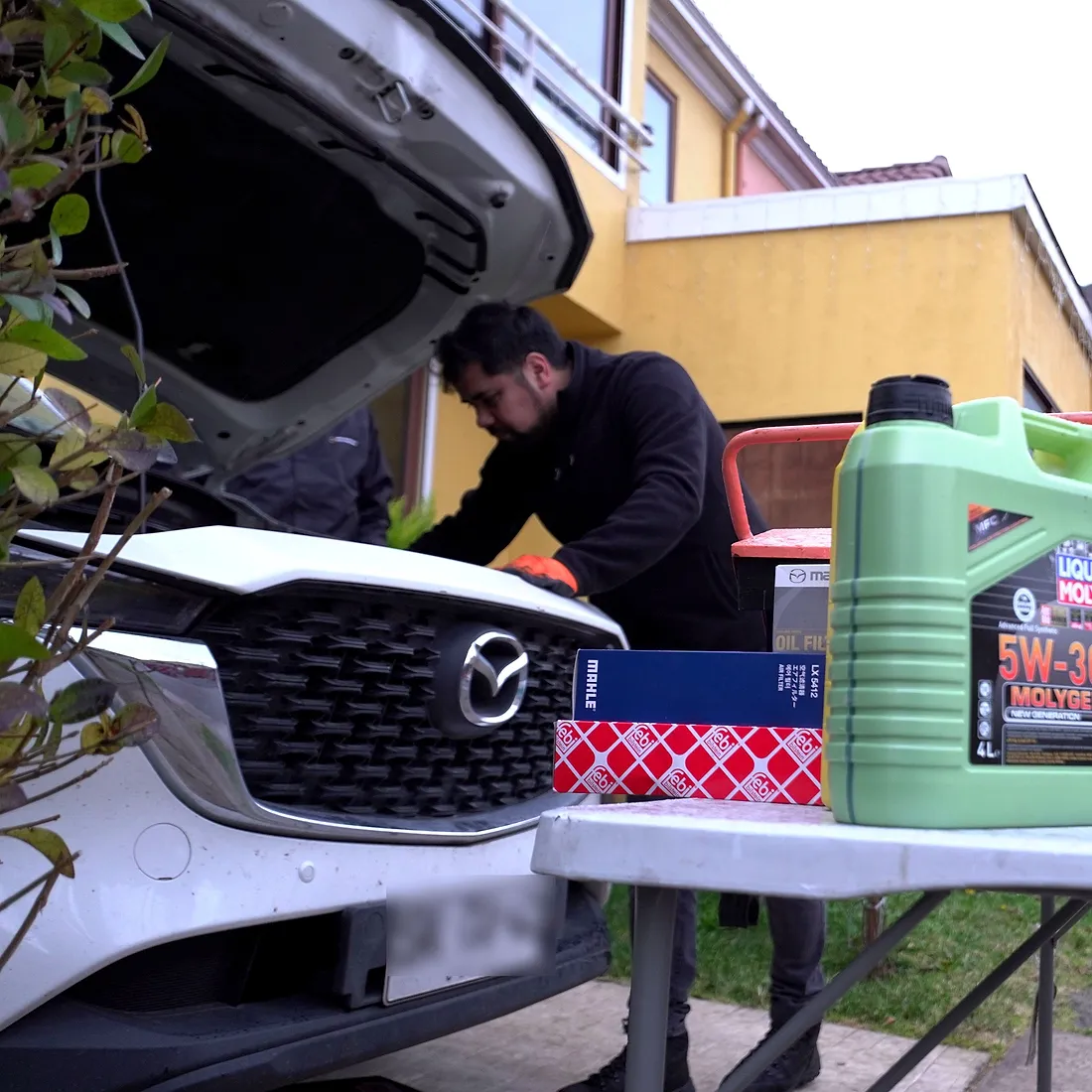Técnico de VALTO realizando una mantención a domicilio sobre un Mazda, con aceite Liqui Moly y filtros originales preparados en la mesa de trabajo