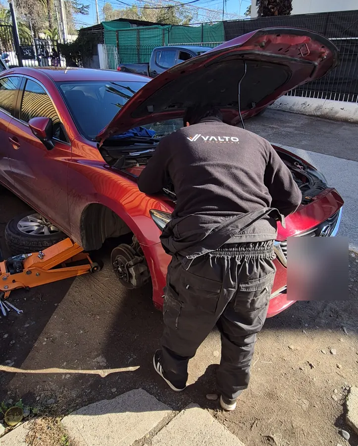Técnico de Valto trabajando en el motor de un Mazda 6 rojo estacionado en la calle